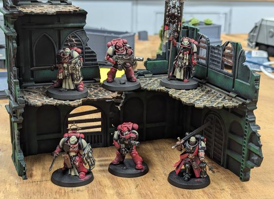 Painted Warhammer 40k minis on a piece of scenery. Six Space Marines painted as Blood Ravens in front of a pair of green ruins.