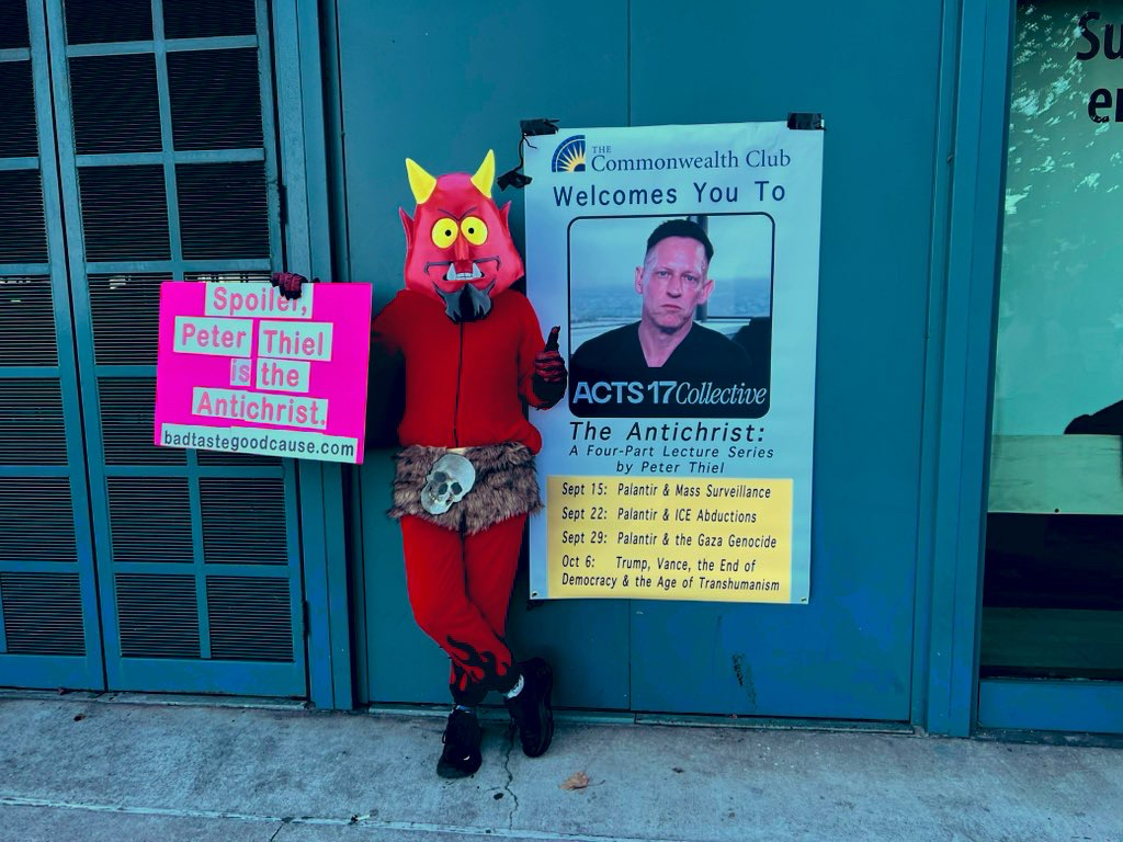 Person in devil costume with anti-Thiel posters