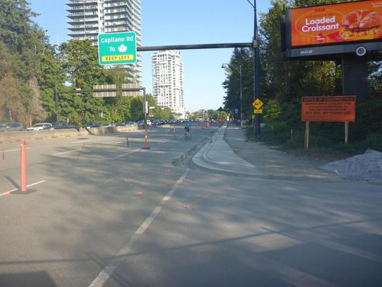 Curbs poured for multi-use-path. Cyclist using part of road blocked for construction.