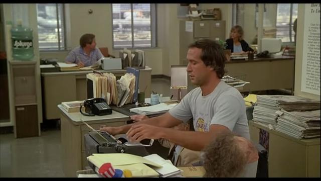 Fletch rolls a sheet of paper into the platen of a Royal HH standard typewriter at his office desk.