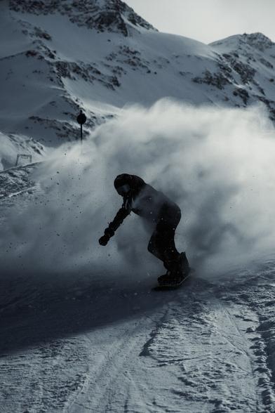 A snowboarder drives through a cloud out of pushed snow he created with his last manoeuvre