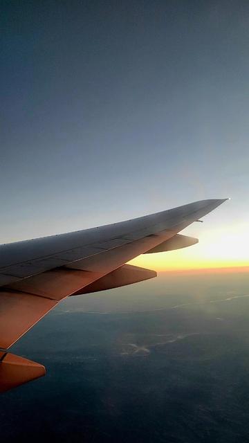 Part of the right wing of a commercial jet aircraft seen from inside the aircraft. Orange light from rising sun falls on the wing.