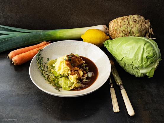 Dunkler Untergrund. Eine helle Schale. Darin: Kartoffelpüree mit gedünstetem Spitzkohl und Rotweinjus