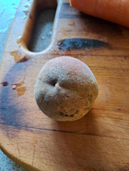 Ein Pfirsich mit dunkler Haut liegt auf einem Holzbrett