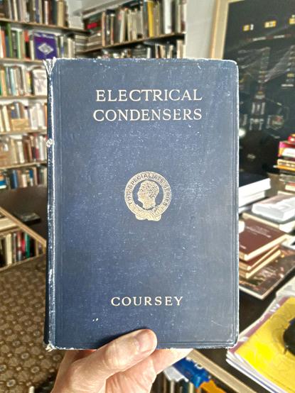 A hand holds a copy of the book "Electrical Condensers" by Philip R. Coursey.