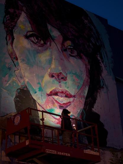 A person on a lift looking up at a mural they are painting