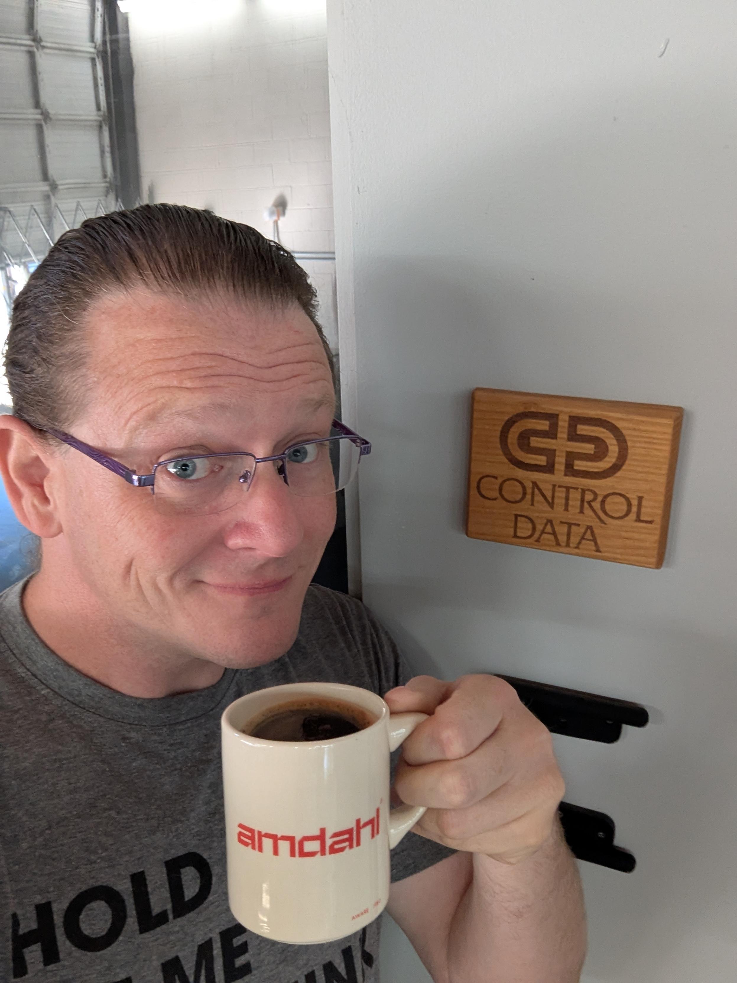 A selfie in front of a conference room sign reading "Control Data" while holding a mug that reads "Amdahl."