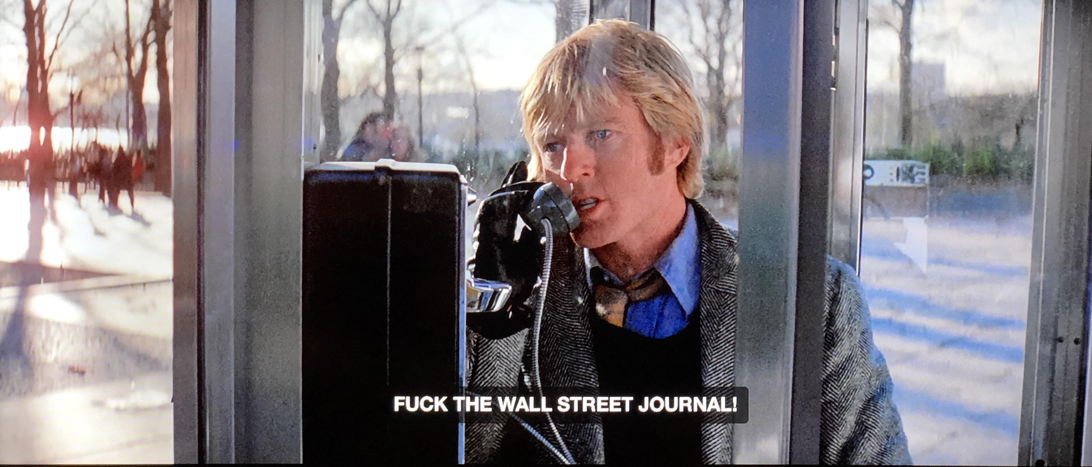 A screenshot from Three Days of the Condor. Looking into a phone booth where an impossibly handsome Robert Redford is snarling ‘FUCK THE WALL STREET JOURNAL!’ Into the handset