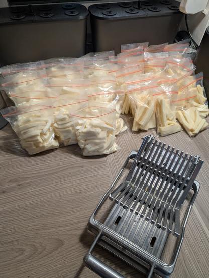 Ein Foto vom Küchentresen, darauf etliche kleine Zippertüten gefülltmit geschnittenem Pizzakäse. Im Vordergrund ist ein großer Mozzarelleschneider aus Metall zu sehen.