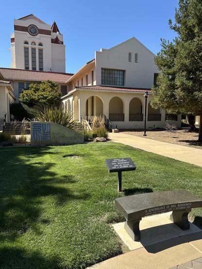 Photograph of the clock tower at the Oracle campus in Santa Clara, California with the historical Sun Microsystems sign and Phil Rosenzweig memorial in the foreground.