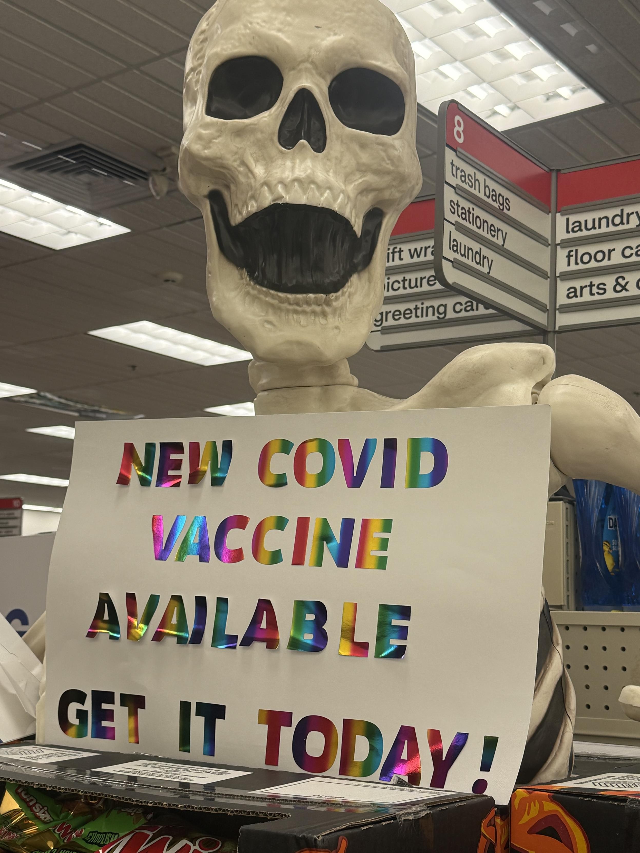 Huge skeleton holding a sign saying “new COVID vaccine. Get it today”