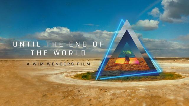 Promotional image for a film. The film title, UNTIL THE END OF THE WORLD, appears above the the line "A Wim Wenders Film". The image is of a desert landscape -- the Australian outback -- with a blue sky containing some clouds above. A green oasis has an abstract series of concentric triangles superimposed above it, in neon and metal, each showing slices of landscapes within; with the inner most triangle showing a vague image of two people standing side by side.