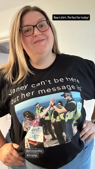 A plus size blonde woman in glasses wearing a tee shirt showing police office high fiving a protester carrying a sign saying "Trump is a runt" the protesters hand is covering the lower part of the "r" in rump so it looks like the letter "c".