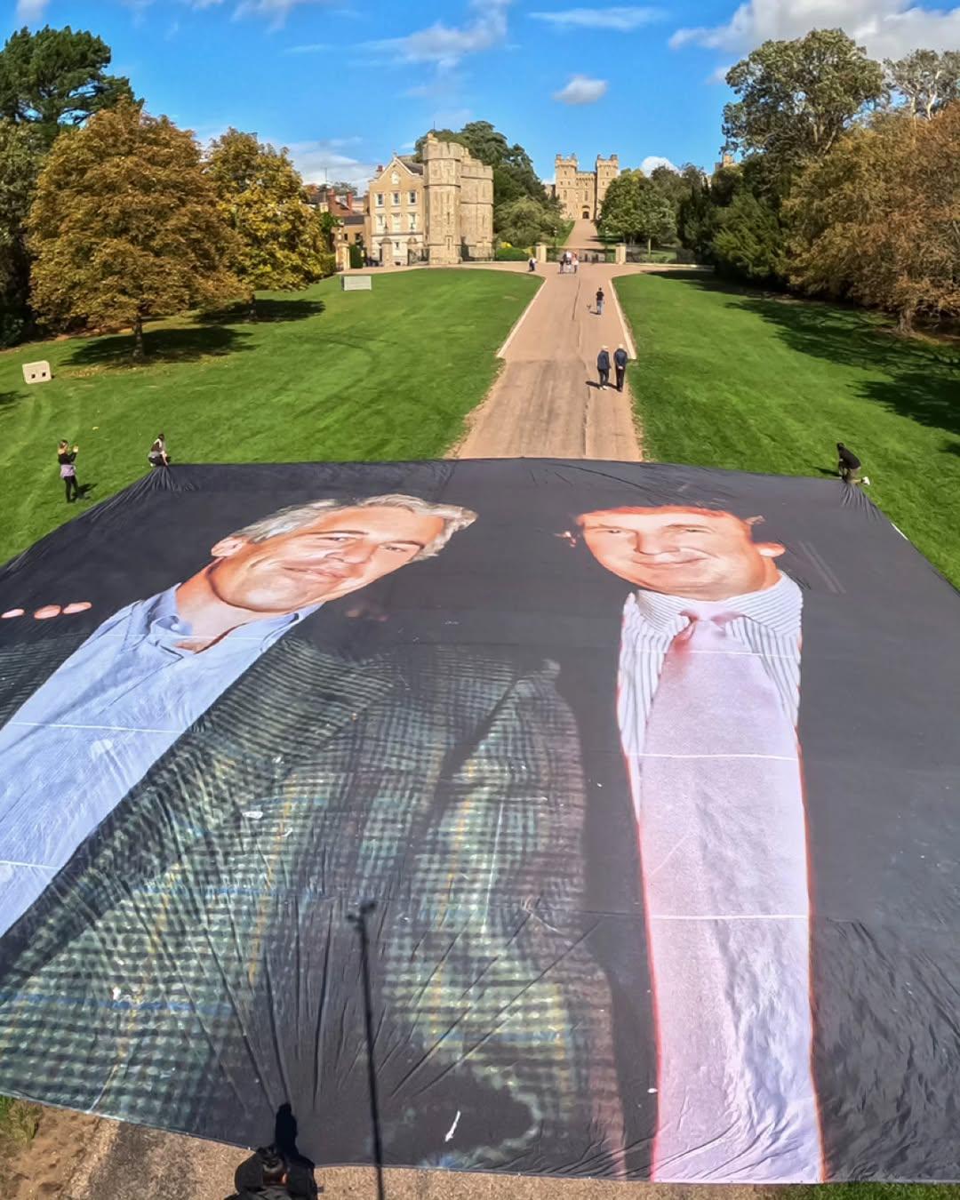 A giant protest banner hangs across from Windsor Castle in England, where Donald Trump is staying with King Charles during his UK visit. The massive banner, funded by 1,770 people, shows the world’s largest printed photo of Trump standing beside convicted sex offender Jeffrey Epstein. The display was created as a satirical response to Trump’s visit, which was intended to polish his public image.