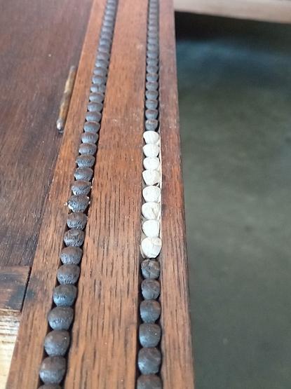 Bei einem Schrank werden im Dekor fehlende Holzperlen ersetzt.
Bild zeigt das bestehende Holzperlendekor als 2 Linien und die Fehlstelle mit neuen, noch hellen Holzperlen, aufgefüllt.