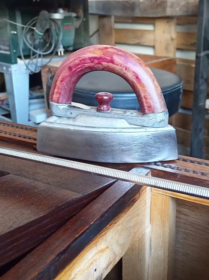 Auf diesem Bild ist ein uaraltes Bügeleisen zu sehen, welches die Holzperlen des vorherigen Bildes fixiert. Die Holzperlen wurden verleimt, das Bügeleisen bringt die nötige Schwere mit.