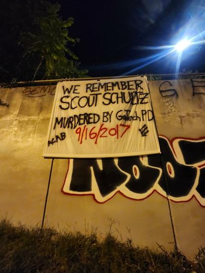 Banner on the side of a bridge that reads "We Remember Scout Schultz murdered by GATech PD 9/16/2017 ACAB"