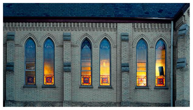 Stained glass windows on the side of a church that are illuminated by the setting sun.