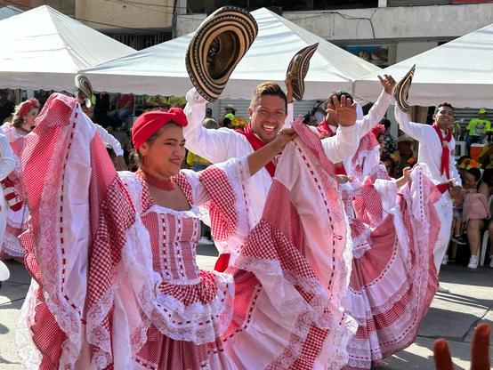 Men and women dancers shown wearing red and white costumes walking.