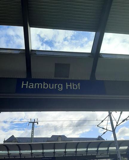 Ein Foto von einem Bahnsteig am Hamburger Hauptbahnhof, im Zentrum des Bildes ist das dunkelblaue Schild mit der weißen Aufschrift "Hamburg Hbf"
