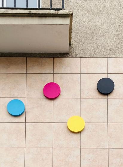 Fassade. Ausschnitt mit Balkon und gekachelter Wand. Auf der Wand vier runde Scheiben in Cyan, Magenta Gelb und Schwarz = CMYK