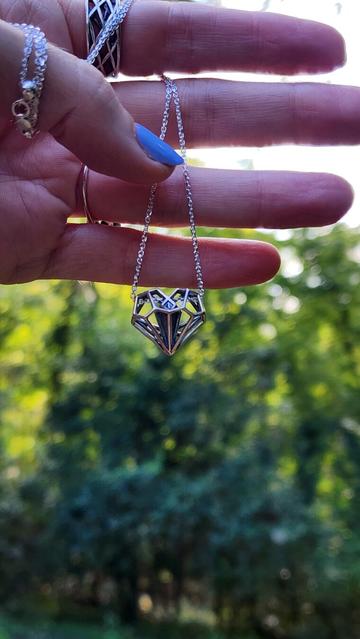 A hand holds a sterling silver geometric heart necklace in the woods during golden hour. This original design by Xover0 is integral to the plot of the Netflix movie Uglies.