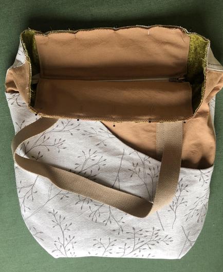 Tasche aus Beigem und braunem Stoff liegt auf einem grünen Tisch. An der oberen Öffnung der Tasche ist ein Panel mit Reissverschluss mit Stecknadeln eingesteckt.