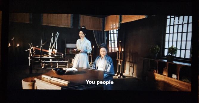 Xueman and mrs Fei talking while a loom set up with red warp stands innocently in the background.