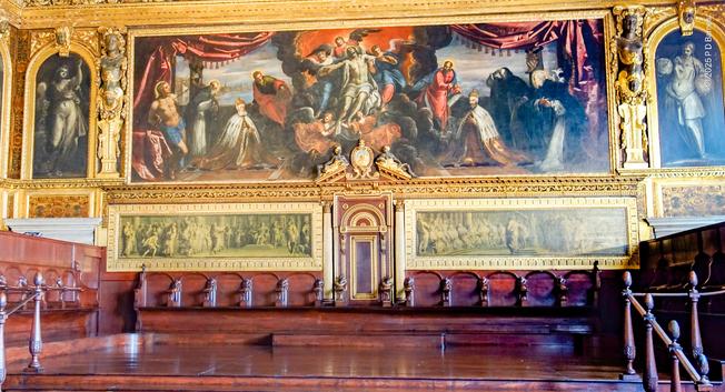 Detail of some of the senate seats in the Doge's Palace, Venice, a row of timber pews beneath a Tintoretto painting of the dead Christ adored by two Doges