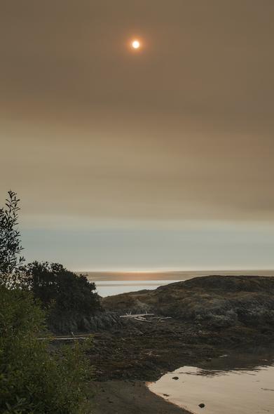 Red rising sun peaking through smoky sky. Lagoon and ocean view.