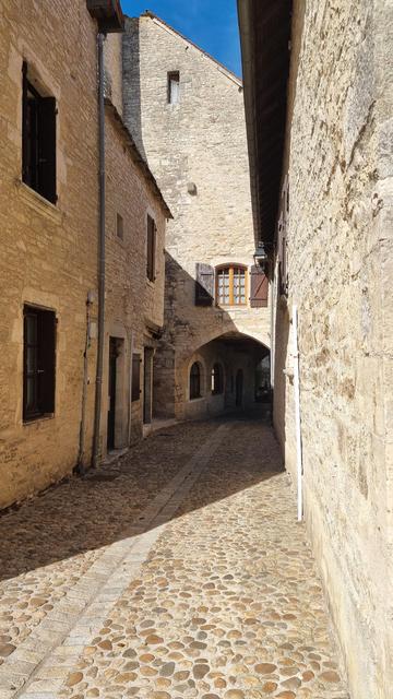 Une rue de Villeneuve de Rouergue avec les maisons en pierre ,une arcade au fond, un jeu d'ombres géométriques