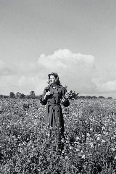 Bergman in a long coat holding flowers in a flowerfield. picture in black and white