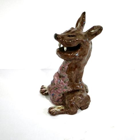 Glänzende Tonfigur. Fantasiewesen mit spitzen Zähnen, Hasenbeinen, rosa Bauch, kastanienbraunem Körper, weißen Pfoten, aufgestellten Ohren, spitzer Schnauze und grinsenden Augen.
