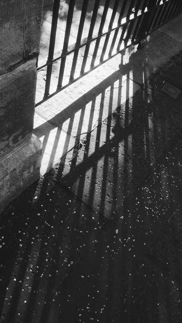 Bars of light and shadows cast through an iron gate by the morning sun