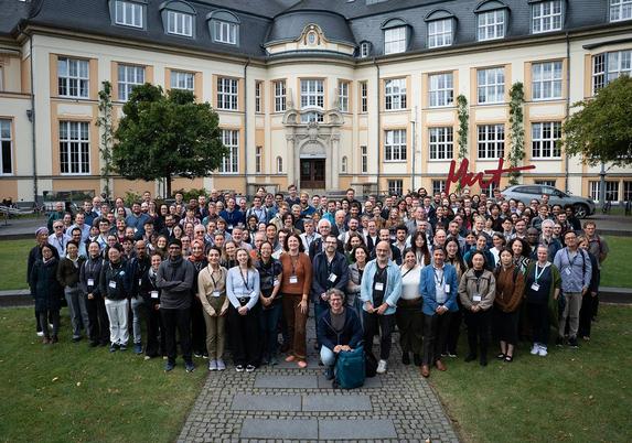 Group photo on the Bucerius Law School campus. Around 200 people are lined up on the lawn and sidewalk in front of an imposing building.