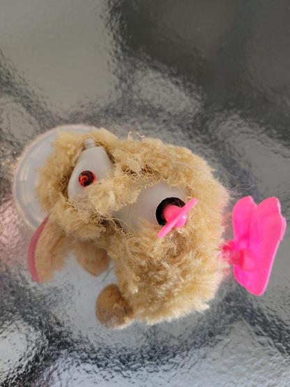 The plush bunny, fallen on a glass table, with torn skin revealing the plastic structure of the head and a red eye. It has a mechanism where it is possible to make the feet move when in a proper position for it.

[pt] O coelhinho de pelúcia, caído sobre uma mesa de vidro, com a pele rasgada revelando a estrutura plástica da cabeça e um olho vermelho. Ele possui um mecanismo em que é possível das corda para que os pés se movam e ele fique pulando, quando em posição adequada para isso.