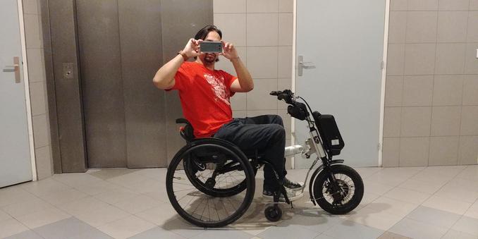 Photo de moi, en fauteuil roulant et handbike électrique,et prenant en photo dans le grand miroir devant un ascenseur. Je tiens le smartphone à hauteur de mes yeux pour les masquer.