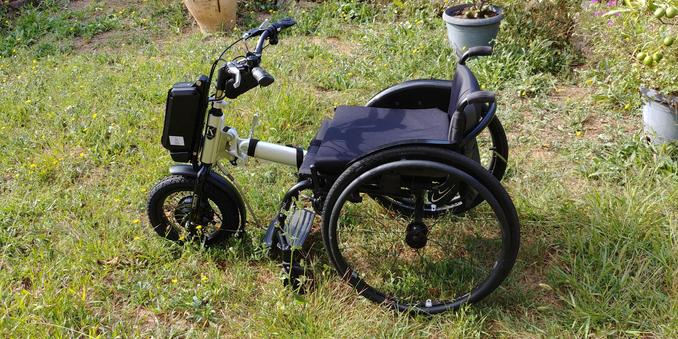 Photo du fauteuil roulant et du handbike électrique, vide, au milieu d'une pelouse touffue.