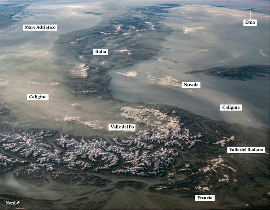 Questa immagine obliqua della penisola italiana, scattata lo scorso aprile con una lente a bassa lunghezza focale da una fotocamera montata all’esterno della stazione spaziale internazionale mentre era in orbita sulla Francia, guarda verso sudest dalle cime innevate delle Alpi alla Sicilia. Nell’angolo in alto a destra è possibile distinguere una colonna di cenere che si leva dalla vetta dell’Etna, distante circa 1.700 chilometri.

La valle del Po appare oscurata dalla caligine, pulviscolo o fumi che rendono opaca l’aria. Diversi studi suggeriscono che questo fenomeno è dovuto soprattutto all’inquinamento industriale. Quando le condizioni atmosferiche sono stabili, lo smog tende ad accumularsi nella parte alta e media della valle. Le montagne circostanti favoriscono la concentrazione della caligine, impedendogli di disperdersi. Il movimento della caligine trasportata dai venti è stato osservato dallo spazio per decenni. In queste condizioni si vedono spesso le masse d’aria cariche di particelle spostarsi sul mare Adriatico verso sud per centinaia di chilometri in direzione della Grecia. Anche sul lato destro dell’immagine è visibile una piccola colonna di caligine, proveniente dalle città della valle del Rodano, che si muove lungo la costa occidentale dell’Italia spingendosi almeno fino alla Sicilia