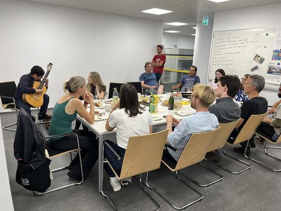 Group gathering around a table while one person plays the guitar.