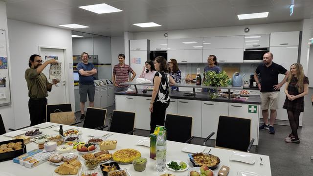 Group gathering in the kitchen. One person just received a farewell-gift.