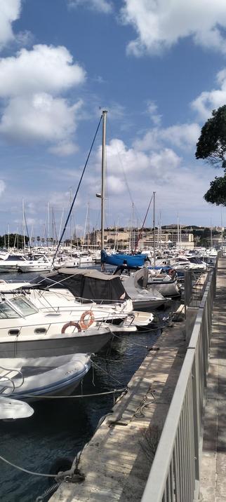 Pieta Marina, central Malta...rows of small yachts and house boats are moored under white fluffy clouds and a blue sky. The limestone walls of Bombi, Floriana are the distance