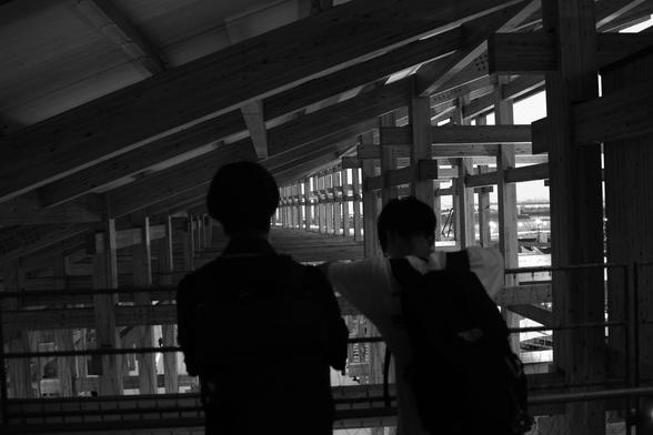 two young men look out under a looming wooden ring, from high up within the structure, their backs to the camera
