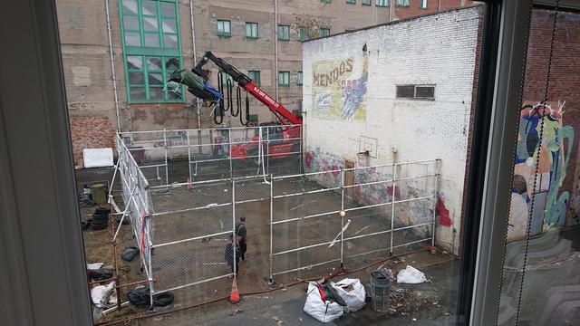 A half-basketball court with chain-link fencing round three sides; the fourth side is the wall of a brick warehouse.

There's a faded sign for Mendos soap painted on the side of the building, and graffiti along the bottom of the wall; and bits of stained paintwork dotted here and there.

All of that has been carefully painted by the set artists, and the whole fence has been constructed and painted over the last day or two.

There's a firefighting hose running along the edge of the court, which is actually for creating the clouds of steam to make the area look like New York (well, Gotham City) and in the background is a large red teleloader which has a seriously large lighting rig on it.