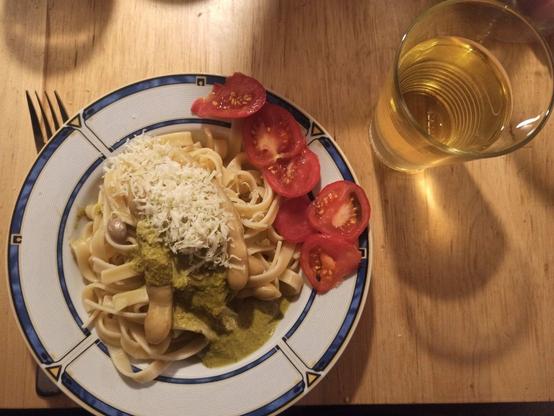 Teller mit Fettucine mit Bohnen und Kartoffeln. Dazu Pesto und frisch geriebener Parmesan und eine in Scheiben geschnittene Tomate aus dem Garten. Daneben ein Glas Weißwein