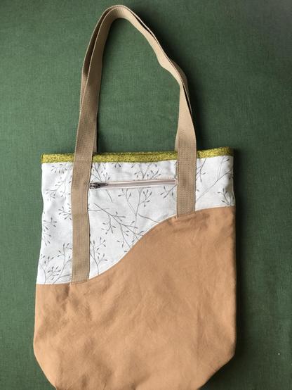 Einkaufstasche mit einer Wellenförmigen Teilung aus Ockerfarbenen um Beigen Stoff liegt auf einem grünen Tisch. Henkel sind auch beige