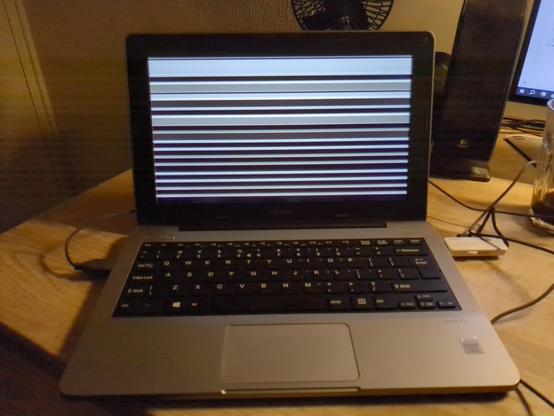 A photo of a small silver coloured laptop computer with its screen showing black and white horizontal stripes.