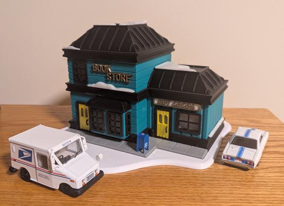 A miniature bookstore with a diecast post office truck and a Corvair parked outside.
