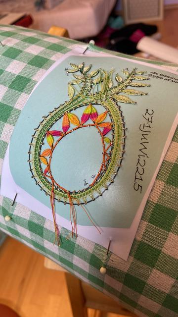 Ein grünes Ei mit vielen kleinen Blättern, noch mit Nadeln auf einer Klöppelrolle befestigt