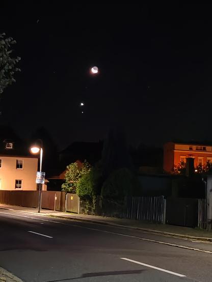 Foto zeigt im Vordergrund Gebäudebund Gartenzaun innerhalb der Stadt und am Himmel die Mondsichel mit Planet Venus unterhalb.